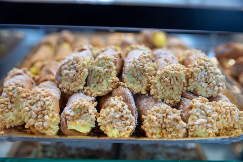 Image shows: a close up view of the display of pistachio cannoli at Caffe Pompei in Stirling. Pastry tubes filled with green pistachio cream and sprinkled with chopped nuts and icing sugar.