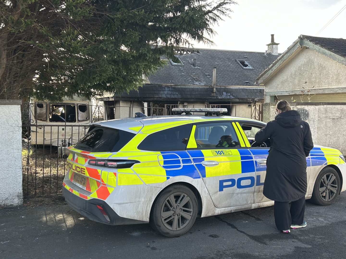 A police car parked at the rear of the gutted house.