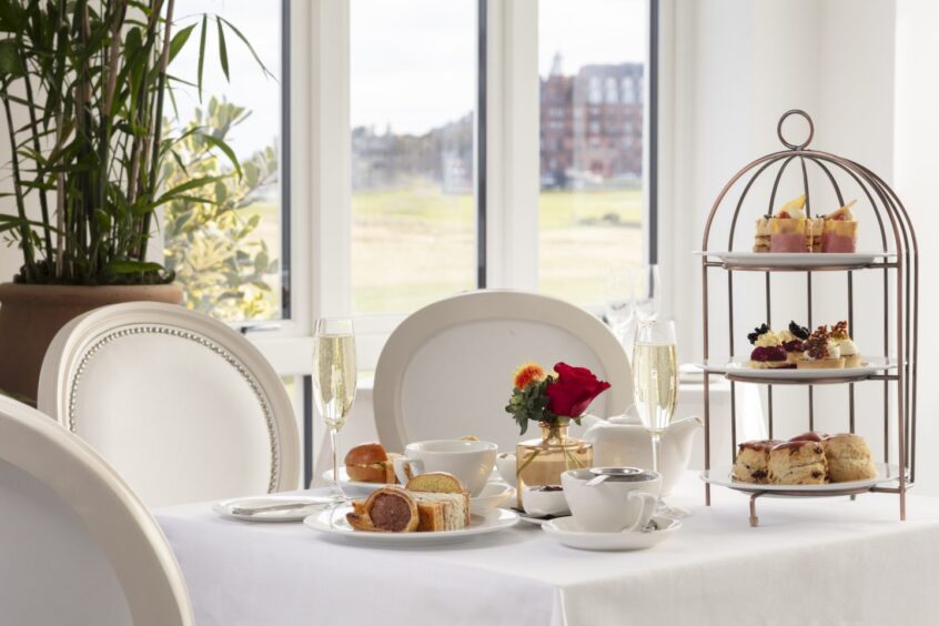 Image shows: a table set for afternoon in the Old Course Hotel, St Andrews. A view of the Old Course and St Andrews can be seen through the windows.