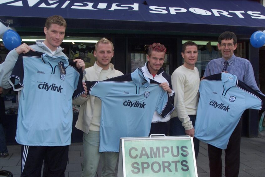 Saints players and a store employee holding up the new Saints shirts outside Campus Sports in 2002