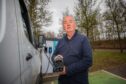 Driver holding EV charging cable up to camera beside white van