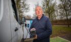 Driver holding EV charging cable up to camera beside white van