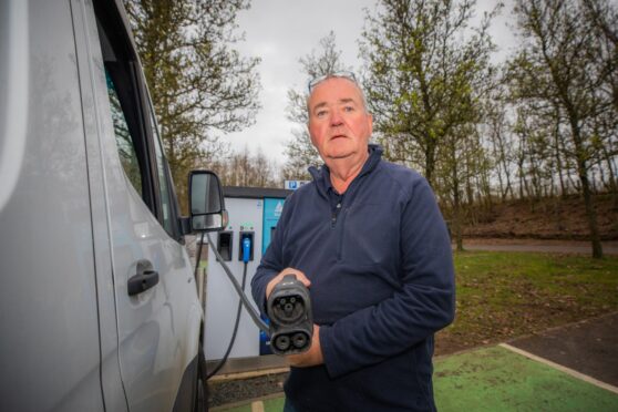 Driver holding EV charging cable up to camera beside white van