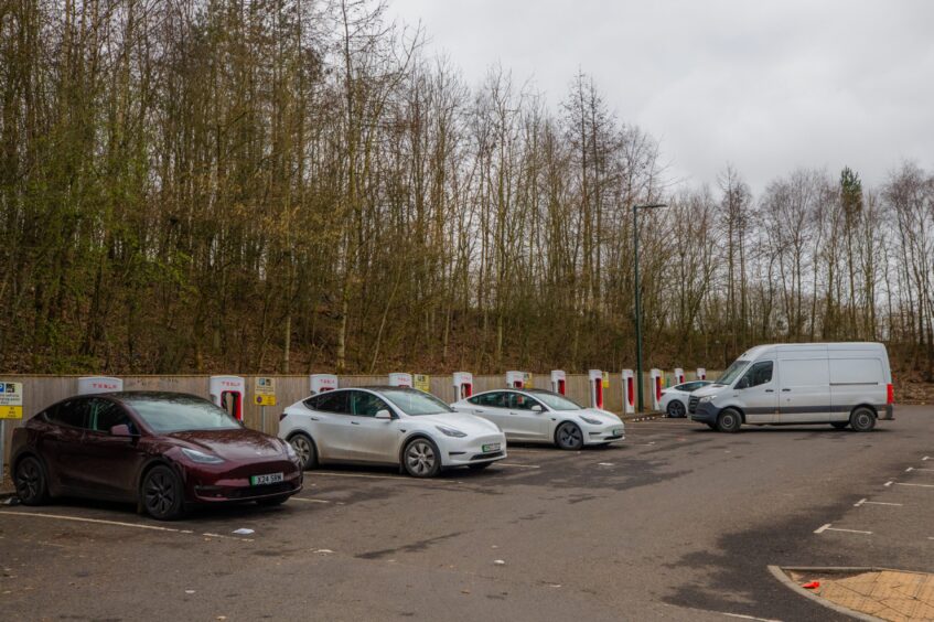 Row of cars at EV charging stations with white van pulling into vacant spot