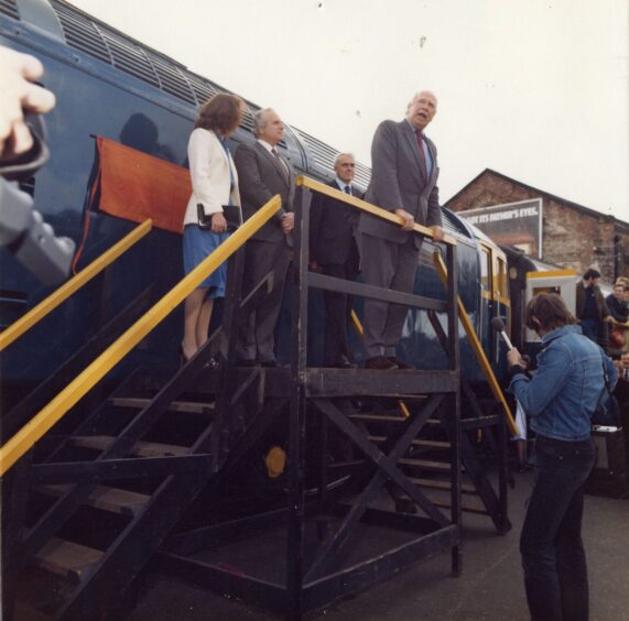 Lord Mackie of Benshie and Joan Ingram speaking on a platform beside the locomotive