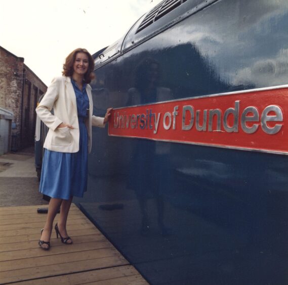 A smiling Joan Ingram beside the University of Dundee train