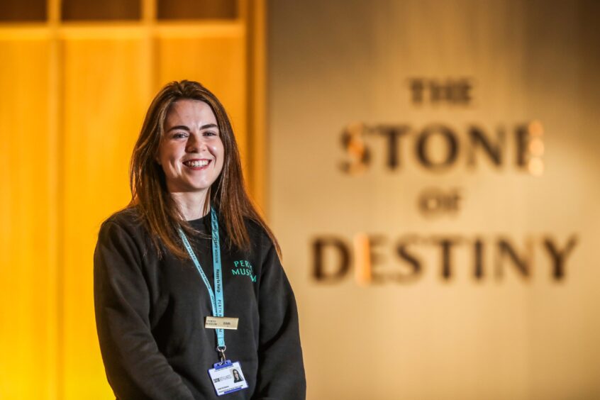 Eilidh McGlashan smiling beside Stone of Destiny exhibit at Perth Museum