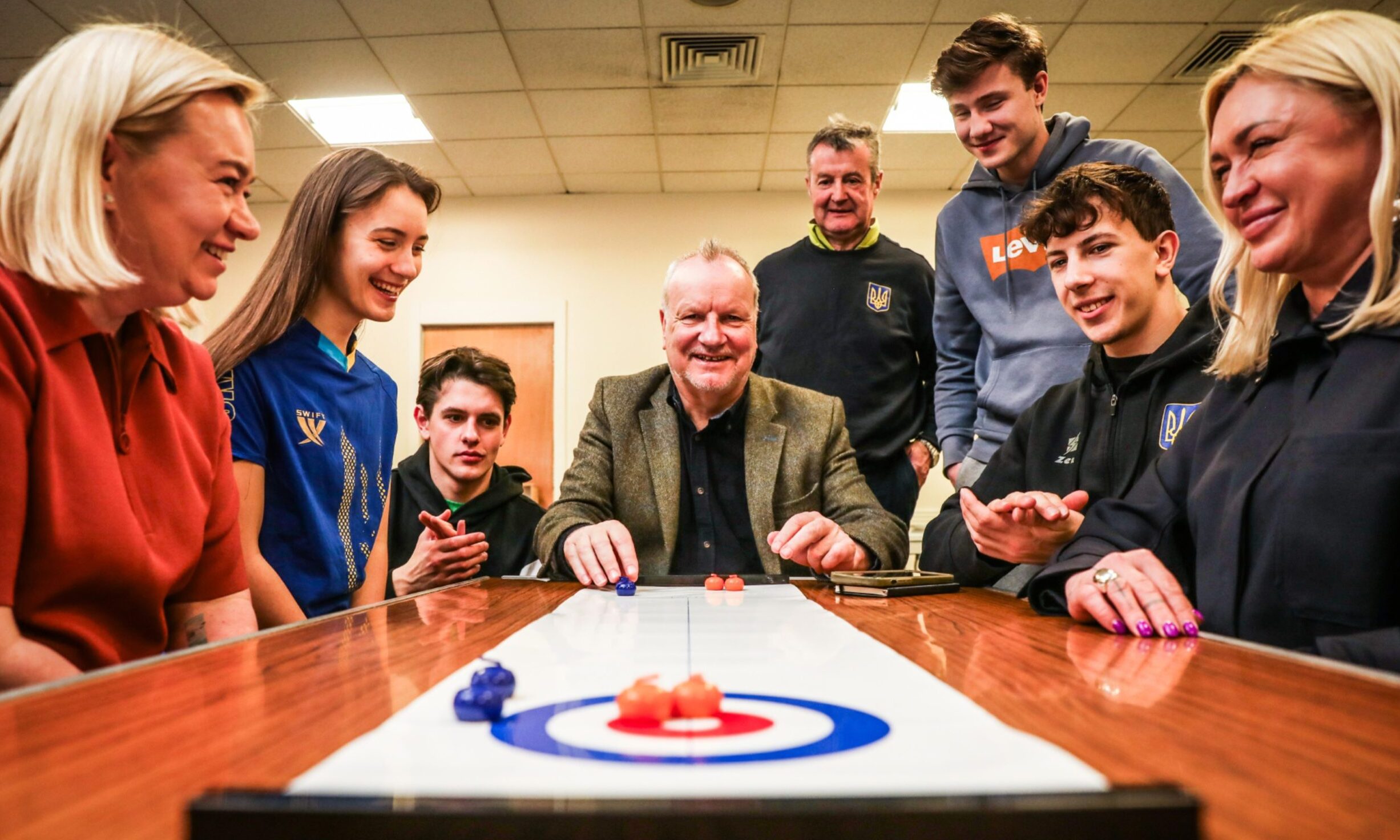 CR0052369, Andy Philip, Perth, Pete Wishart MP as he meets members of the Ukrainian national curling team who have settled in Perth, Picture shows; Pete Wishart MP plays a small more manageable version of curling up in the cafe with the team plus managers and their coach. Friday 7th March, 2025. Image: Mhairi Edwards/DC Thomson