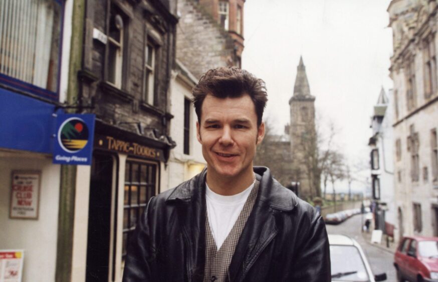 Stuart Adamson in a Dunfermline street in 1996, with buildings in the background, including his pub, Tappie Toories