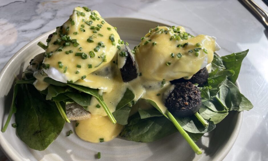 Hebridean eggs come with two poached eggs covering in yellow hollandaise sauce on a bed on small round slices of black pudding and on two slices of toast with fresh spinach.