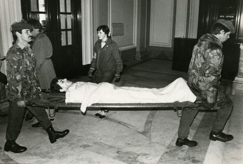 A competitor is stretchered into the Caird Hall by two men in combat fatigues and berets