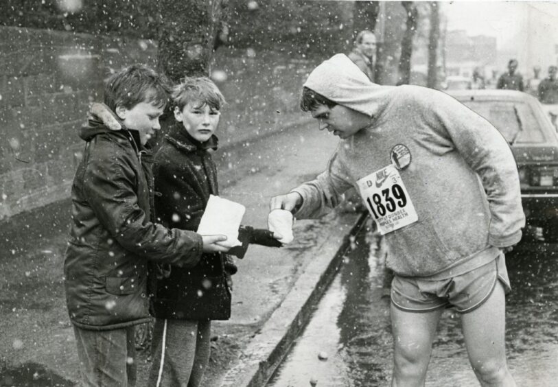 Two boys hold out small paper bags as runner stops for a treat in the snow