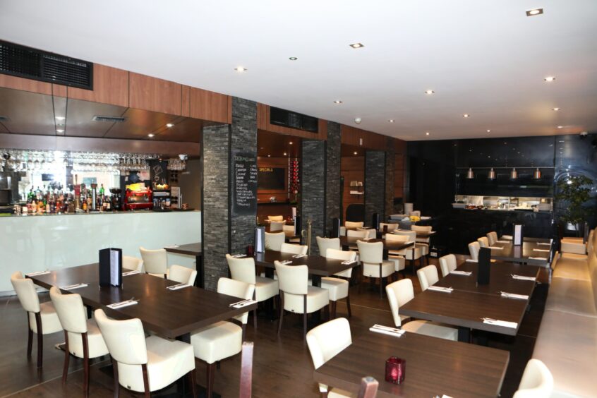 Rishi's restaurant with white seats and dark brown tables and an open kitchen.