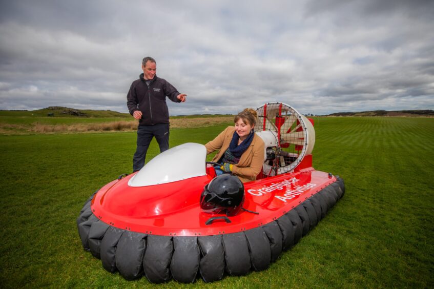John Graham stands next to the hovercraft while Rebecca holds the steering wheel.