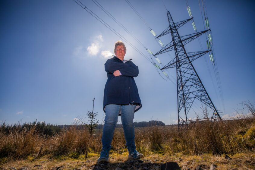 Ruth Kirton, arms folded, standing on moorland next to electricity pylons