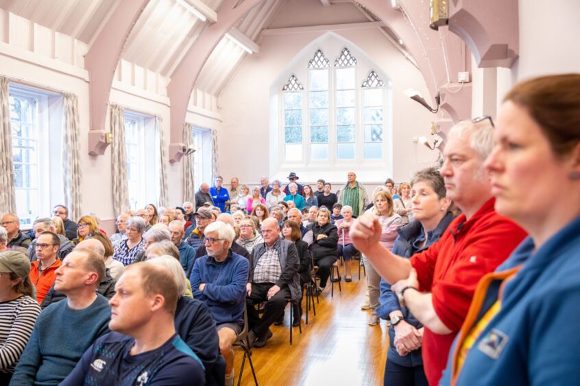 Large group of people seated in rows of chairs at meeting in Errol Village Hall