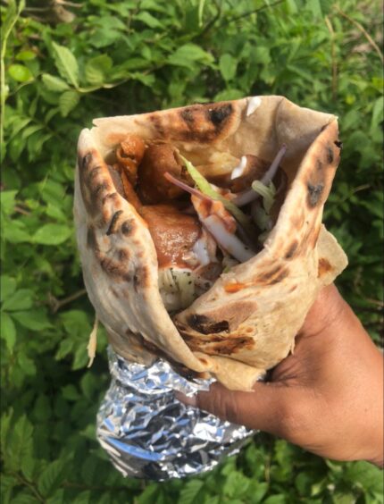 A hand holds a large naan bread wrap containing curry.