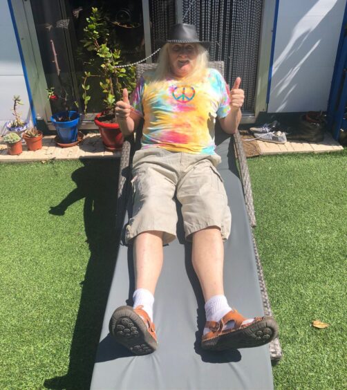 Scott Goring lying on garden furniture with tie-dye t-shirt and cowboy hat, giving two thumbs up