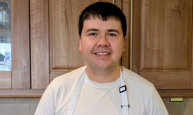 Dundee dad Aaron Mackie wearing Very Good Baking Company apron at home