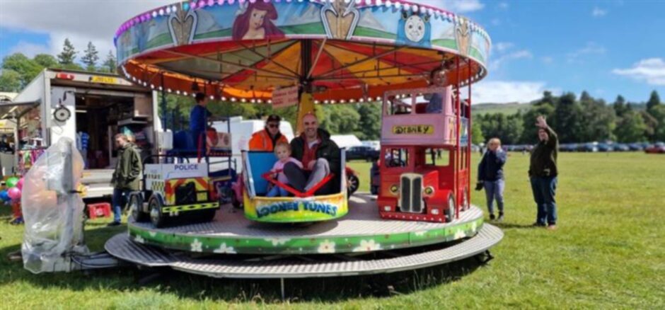 A man and his daughter sit smiling on a children's fairground carousel.