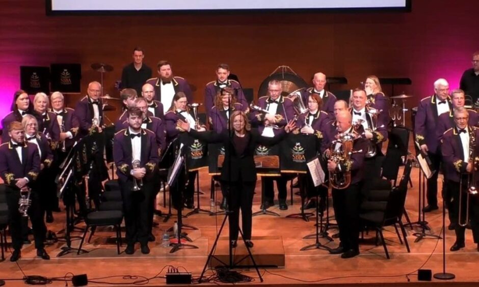 Image show Kingdom Brass band on stage. They are wearing their purple band uniforms.
