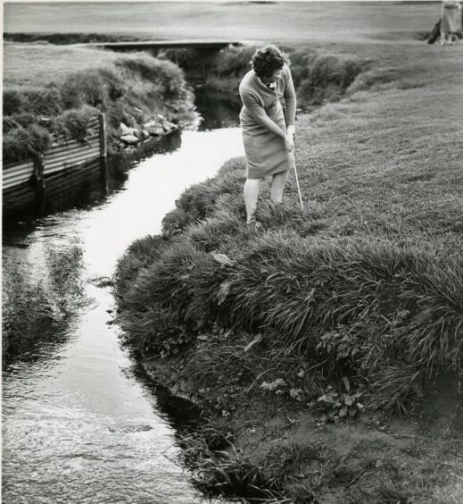 Black and white photo of Jessie Valentine playing golf beside stream