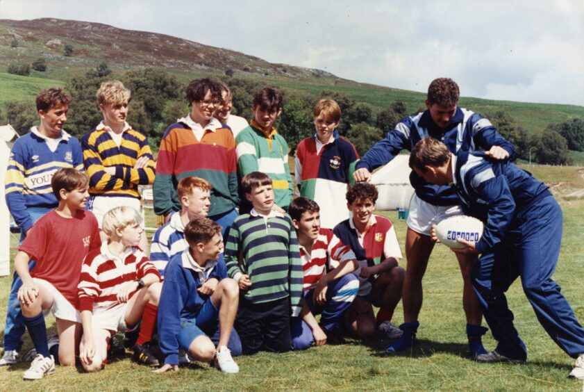 two men put on a tackling demonstration while a group of youngsters looks on