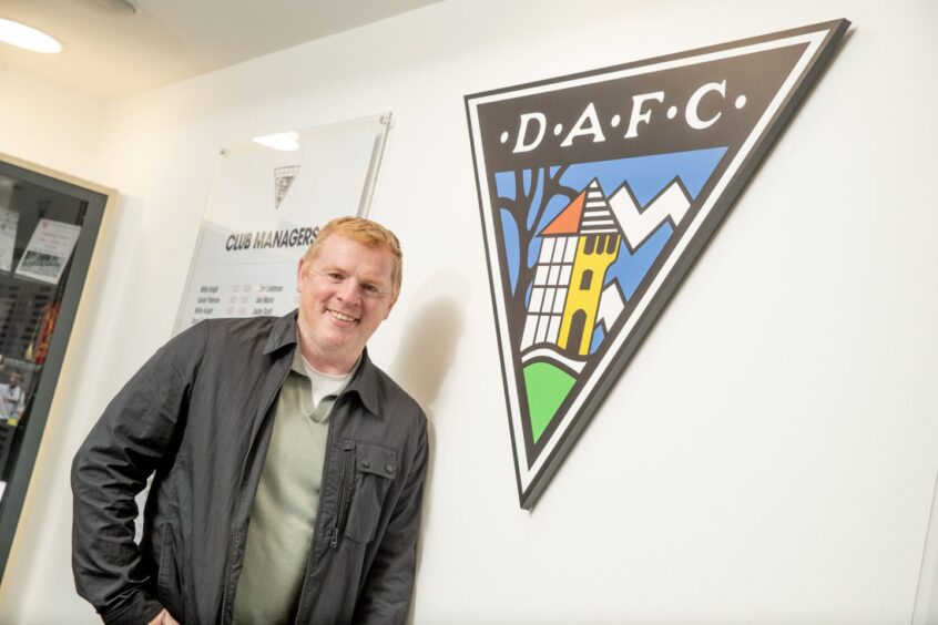 Neil Lennon stands beside a large DAFC badge on the boardroom wall.