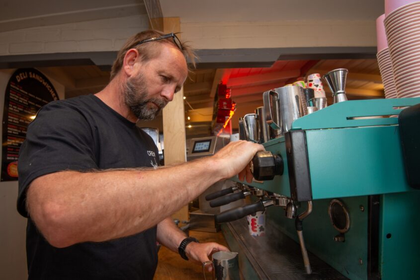 A man in a black T shirt pours coffee from a commercial coffee machine.