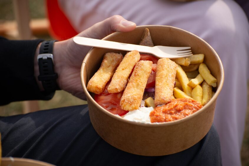 A brown cardboard tub with fries, red sauce and white sauce and long chunks of fried halloumi.