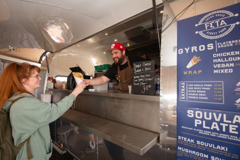 A man in a red cap hands food out to a customer at a silver food truck.