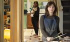 Image shows: Artist Caroline Walker standing in front of one of her paintings. Caroline is based in Inverkeithing. She is wearing an artist's apron and holding paintbrushes. The huge canvas behind her is of a mother holding her baby in a kitchen scene.