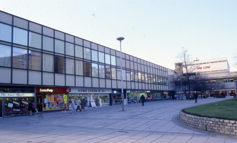 An old shopping centre in 1987, with people walking past the shop windows