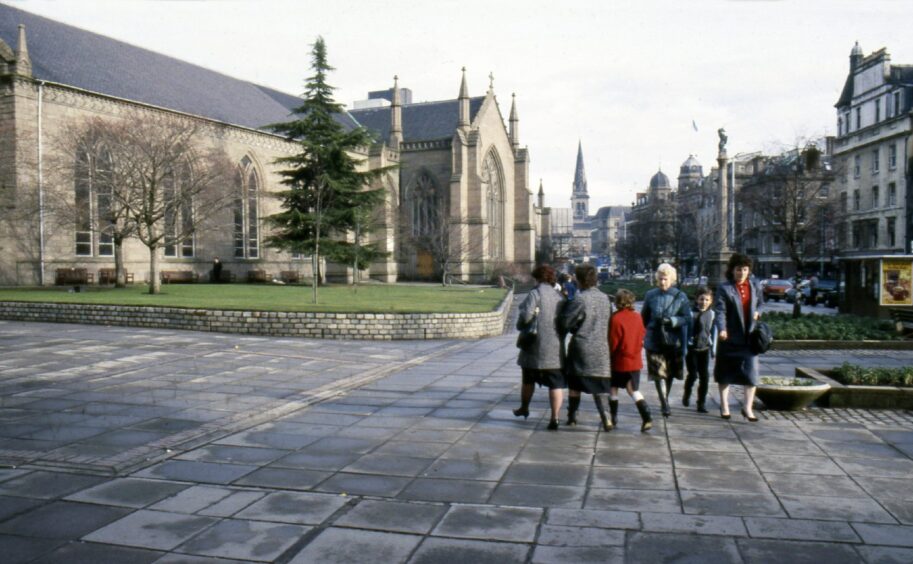 People walking along a street past churches in Dundee.