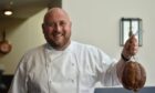 A chef smiling and holding up some charcuterie.