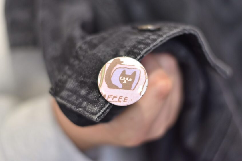 A coffee-themed badge, pinned onto a dark denim jacket.