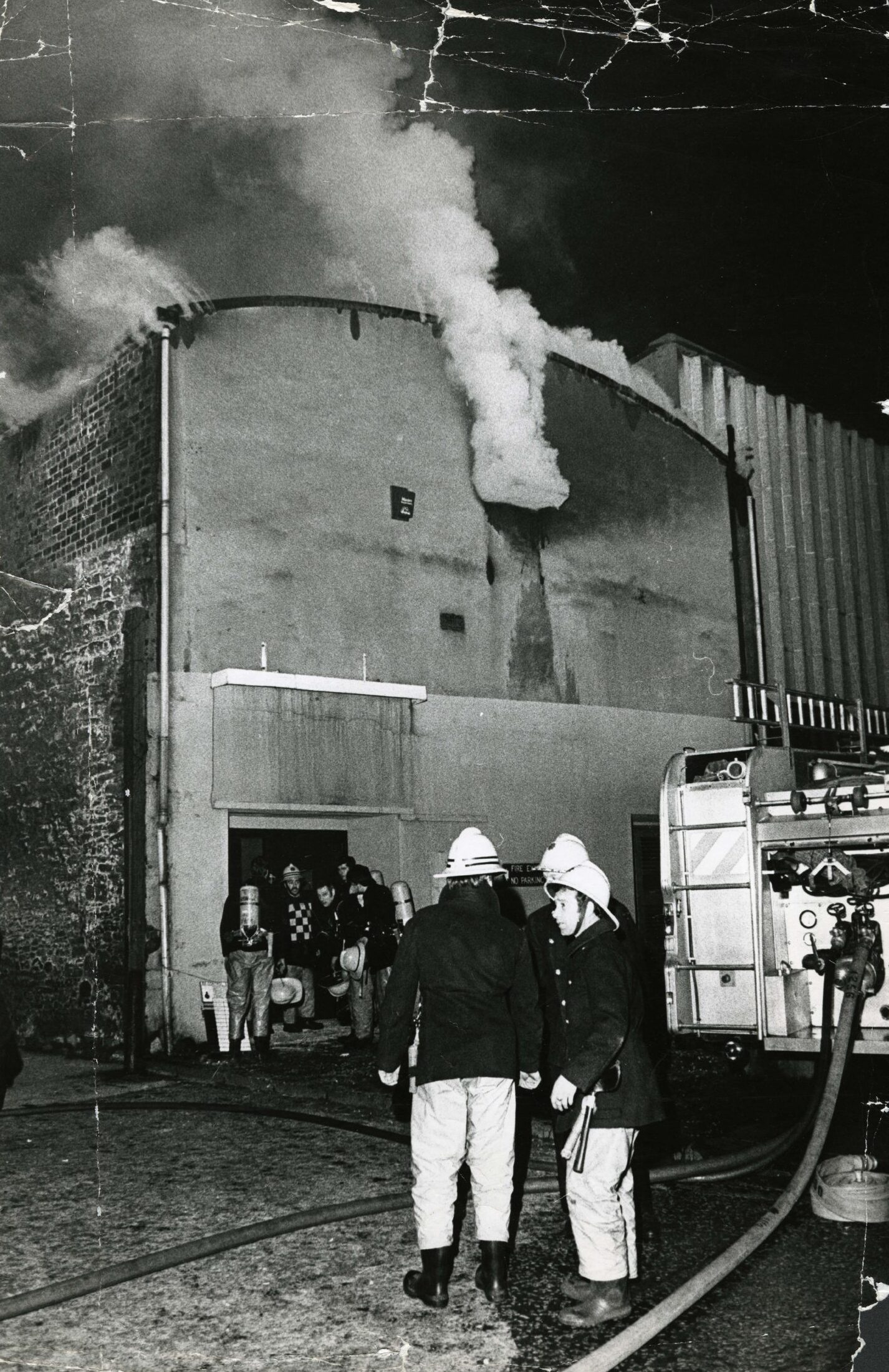 Firefighters beside a fire engine and at the Marketgait entrance to the old Palais, while smoke pours out of the building over their heads.