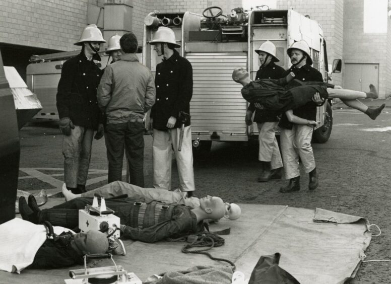 Firefighters beside a fire engine during a mock disaster. They are using dummies laid out on the ground.