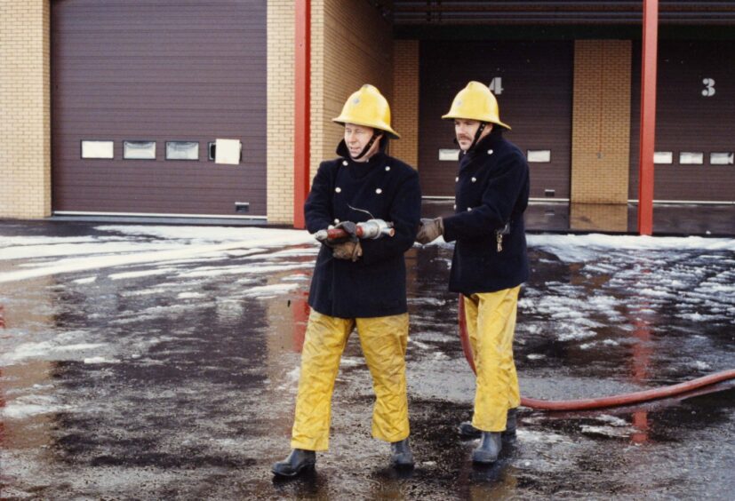 2 Dundee firefighters carry out a training drill with a fire hose in front of a fire station