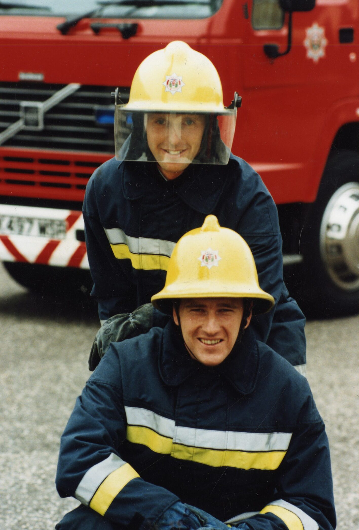 Firefighters Bruce Henderson and Fraser Cochrane, both in helmets, in front of a fire engine . 