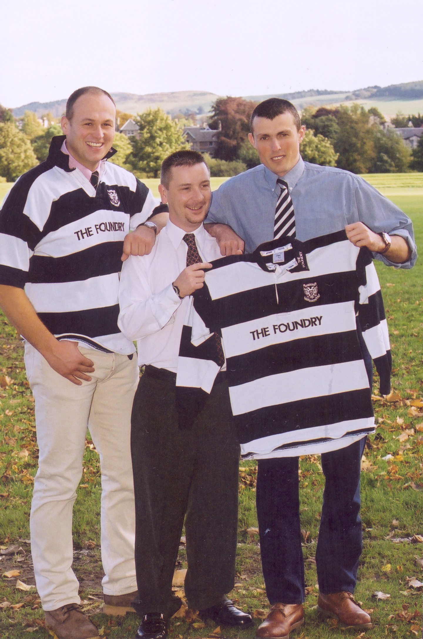 Andy Sinclair, Gordon Brown and Rob Hughes pictured outside and holding up a rugby shirt.