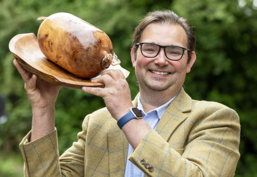 Nigel Ovens smiling, holding wooden sculpted haggis on plate