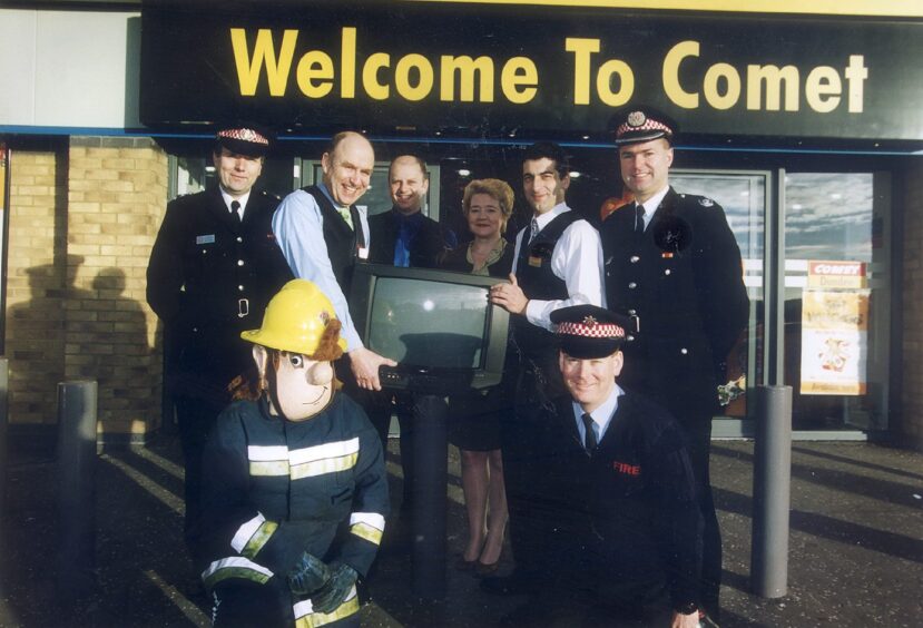 firefighters, one dressed as Fireman Sam, and shop staff, two of whom are holding a TV, outside the Comet store