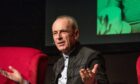 Image shows: Status Quo guitarist Francis Rossi sitting on a red sofa talking to an audience.