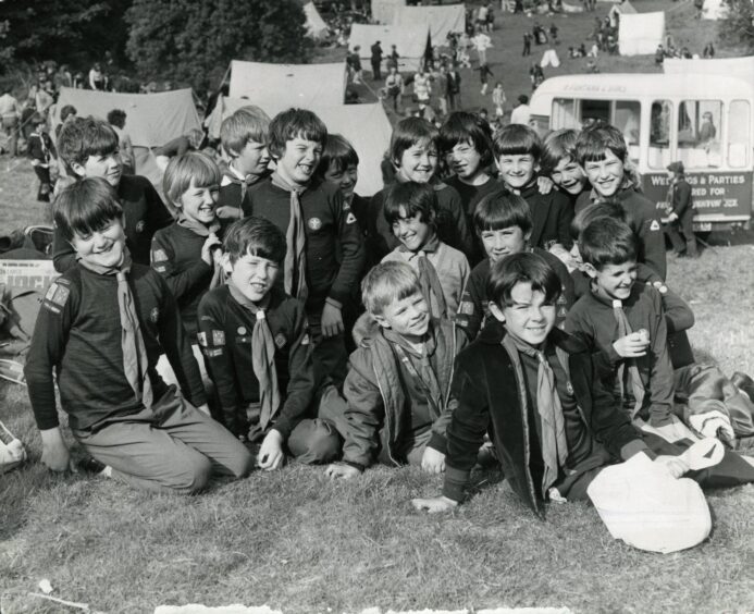 A group of young Scouts, there are several tents and people visible in the background. 