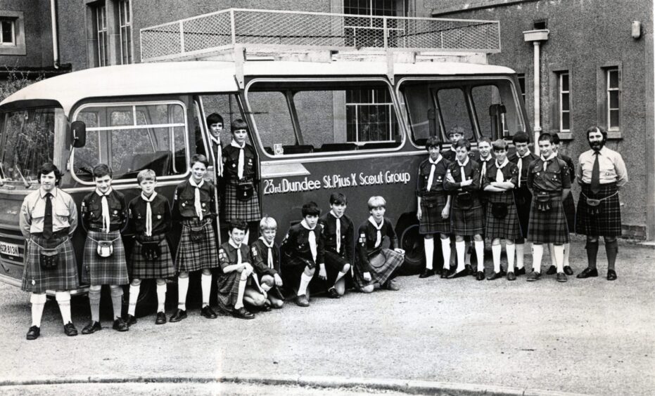 Scout members in kilts lining up in front of the bus