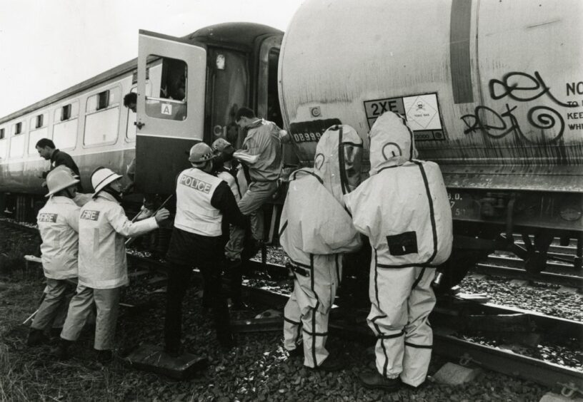 emergency services workers, two in hazmat suits, help someone from a train in a simulated rail crash between a passenger train and chemical-carrying tanker