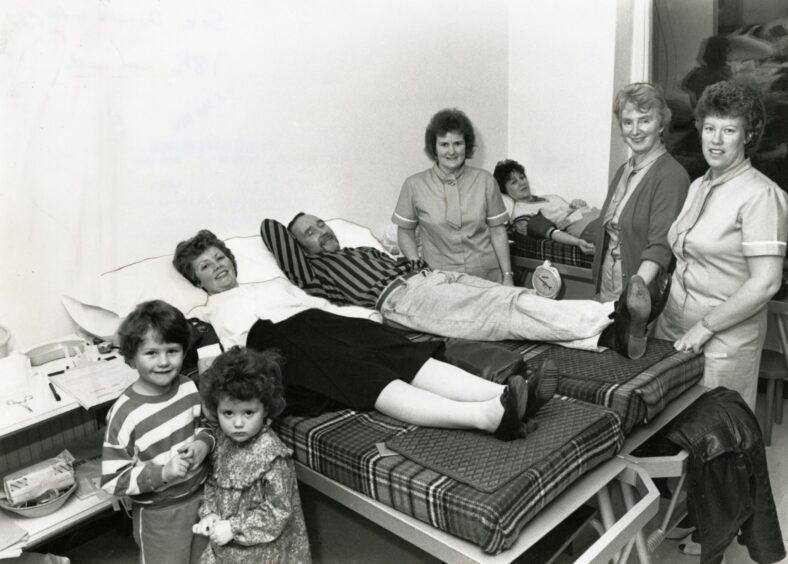 three people lying on beds to give blood. There are two children and staff members in the room also
