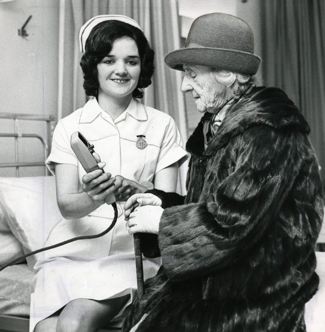 Mary Stewart, 97, being shown around by staff nurse Rena Smith. The pair are sitting on a hospital bed.