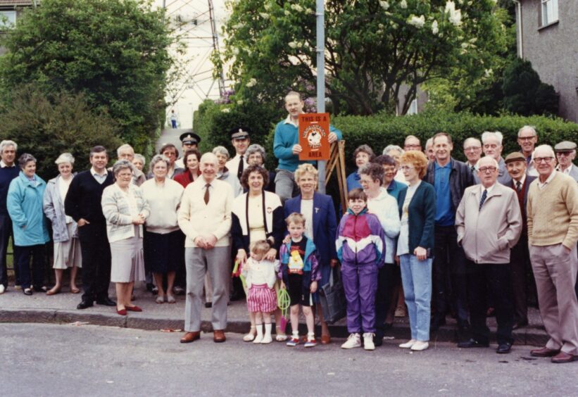 adults and kids gather on the pavement as a Charleston Neighbourhood Watch sign goes up on a lamppost in May 1991.